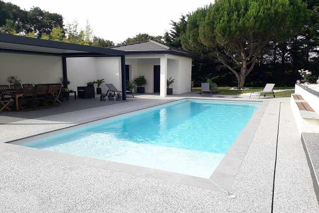 Une piscine rectangulaire avec banquette et escalier immergés et une plage
